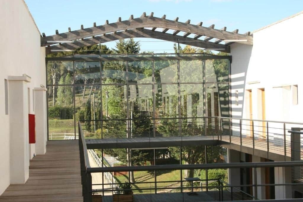 Un edificio moderno con fachada de vidrio, terraza de madera y zona de estar al aire libre.
