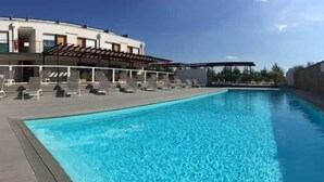 A swimming pool with lounge chairs and a covered area, adjacent to a building with a flat roof and a wooden fence.