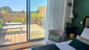 A room with a large window, a bed with green and white bedding, a chair, and a small table.
