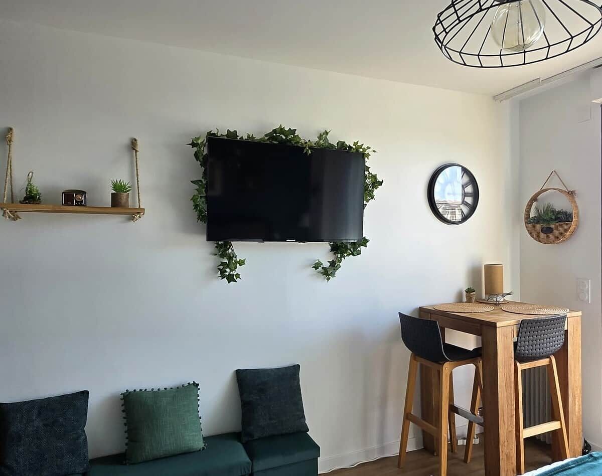 Un salon comprenant un canapé, une table à manger avec des chaises, un téléviseur à écran plat fixé au mur et un luminaire suspendu.