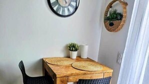 A dining area with a wooden table, two chairs, a wall clock, a small potted plant, and a woven basket.