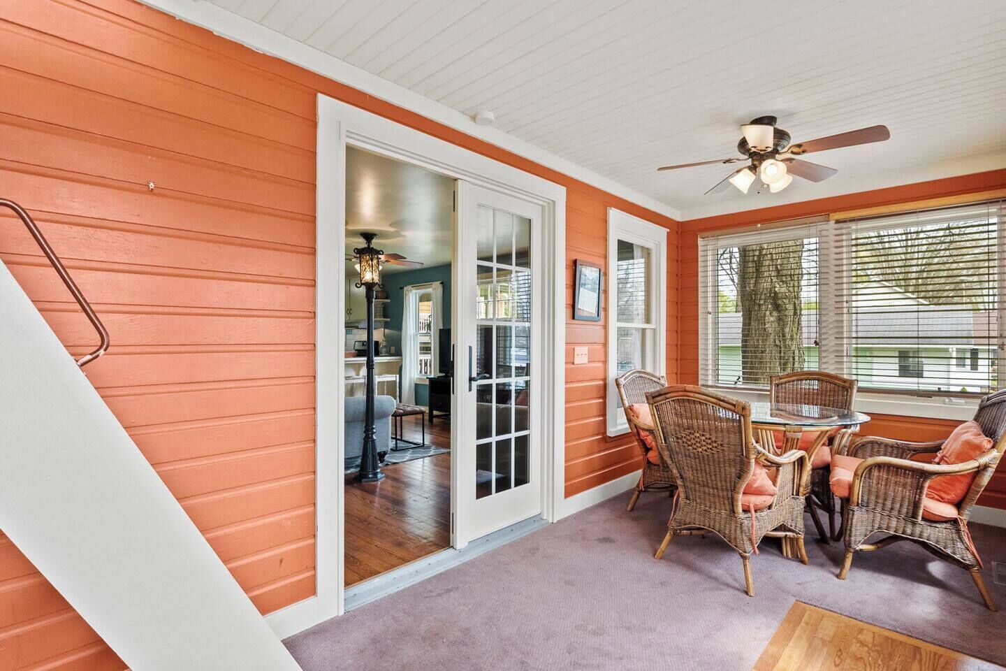 A room with a ceiling fan, wicker chairs, a table, and a view through a window.