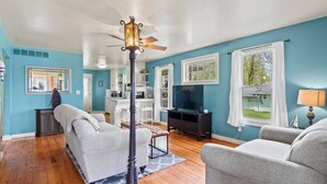 A living room with a ceiling fan, a TV, and a dining area with a kitchen in the background.