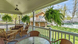 A covered patio with wicker furniture, a glass table, and hanging plants.