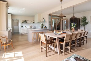 A spacious kitchen with a central island, wooden dining table with chairs, and pendant lighting. - Calamansack Waterings - Sleeps 12 in 6 Bedrooms on the Helford River (Port Navas)