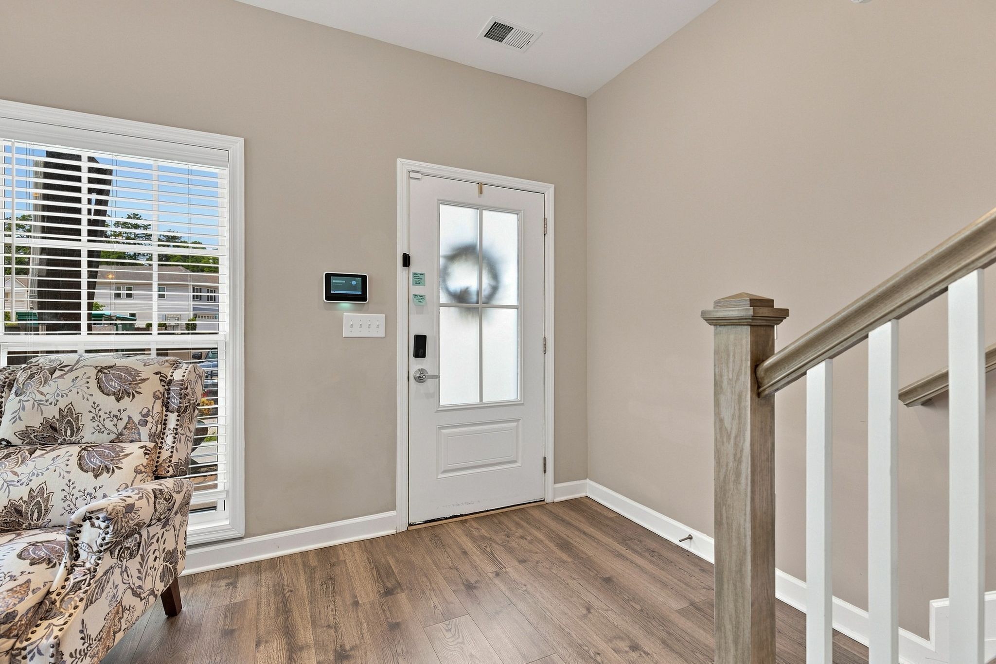 A hallway with a wooden floor, a white door with a window, and a staircase with a wooden railing.