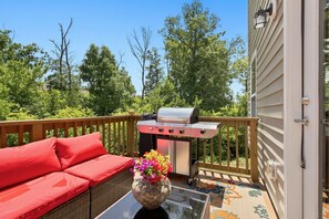 Eine Terrasse mit Grill, einem roten Sofa und einem Blumenvasen.