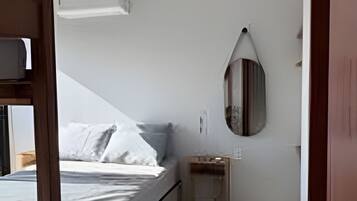Quarto com cama, mesa de cabeceira, espelho e porta.