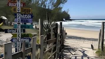A beachside wooden boardwalk leading to a sandy beach with a signpost indicating directions to various locations.