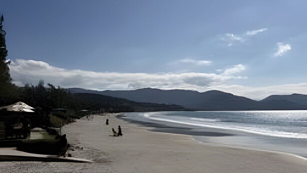A beach with a wooden boardwalk, a few people walking, and distant mountains. - Vista Mar Riviera - Terraço com Vista para o Mar a 50m da Praia da Ferrugem (Garopaba)