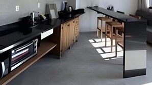 A modern kitchen with a long countertop, wooden cabinets, and a built-in oven. - Vista Mar Riviera - Terraço com Vista para o Mar a 50m da Praia da Ferrugem (Garopaba)