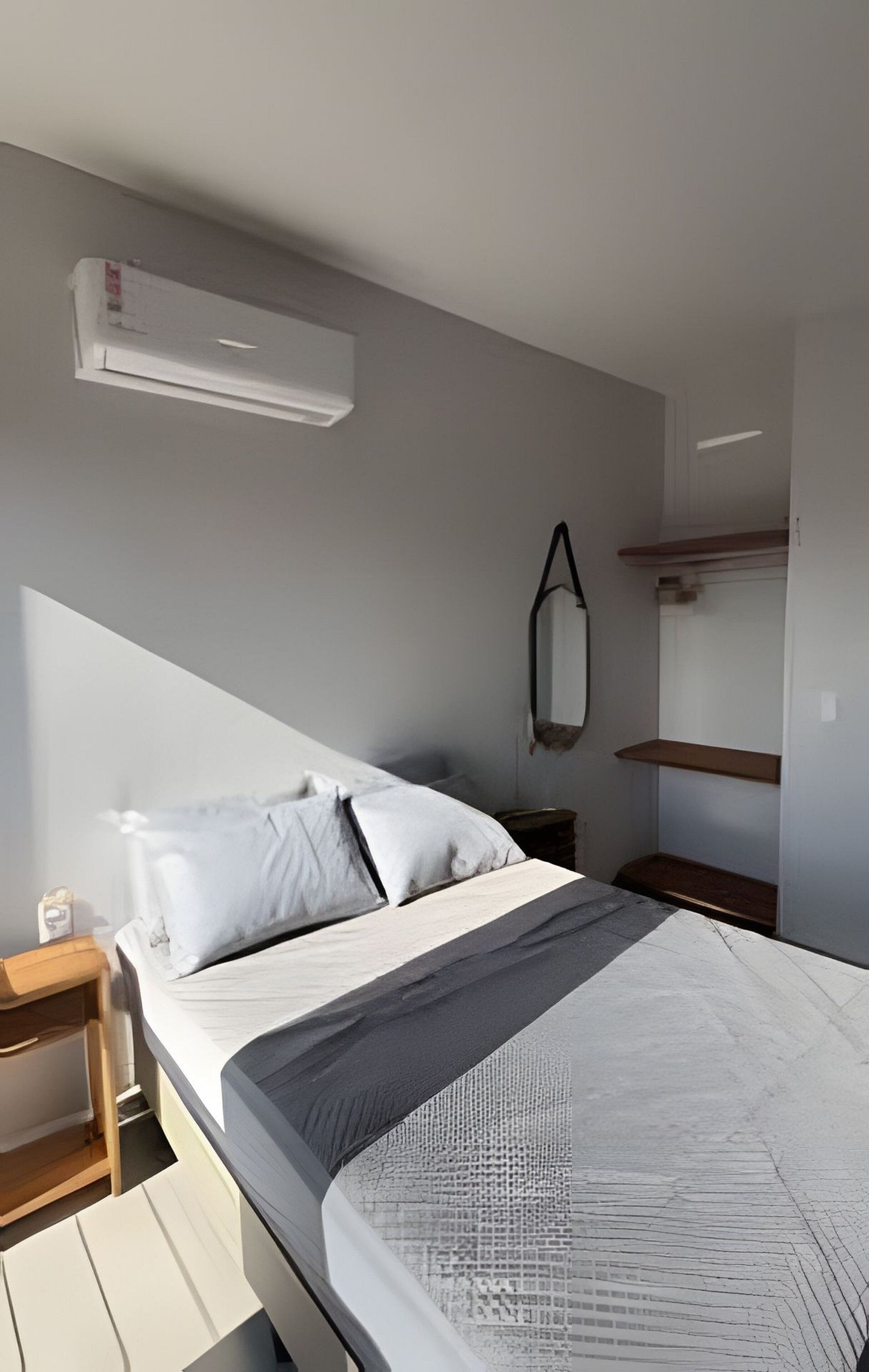 A bedroom with a bed, a nightstand, a wall-mounted air conditioner, a mirror, and built-in shelves.