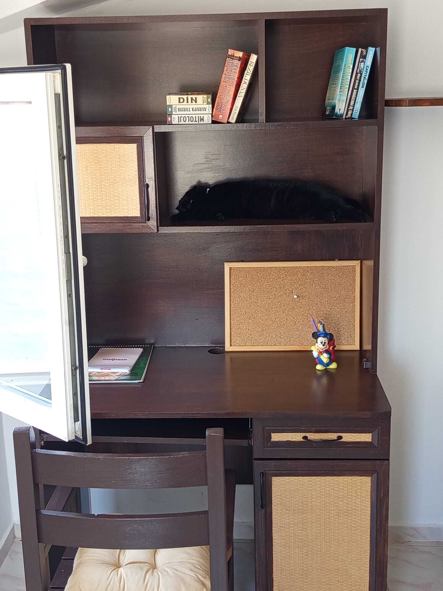 A dark wooden desk with a corkboard, a small Mickey Mouse figurine, and a laptop.