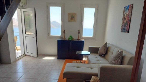 A living room with a sofa, a small table, a cabinet, and a view of the sea through a door.