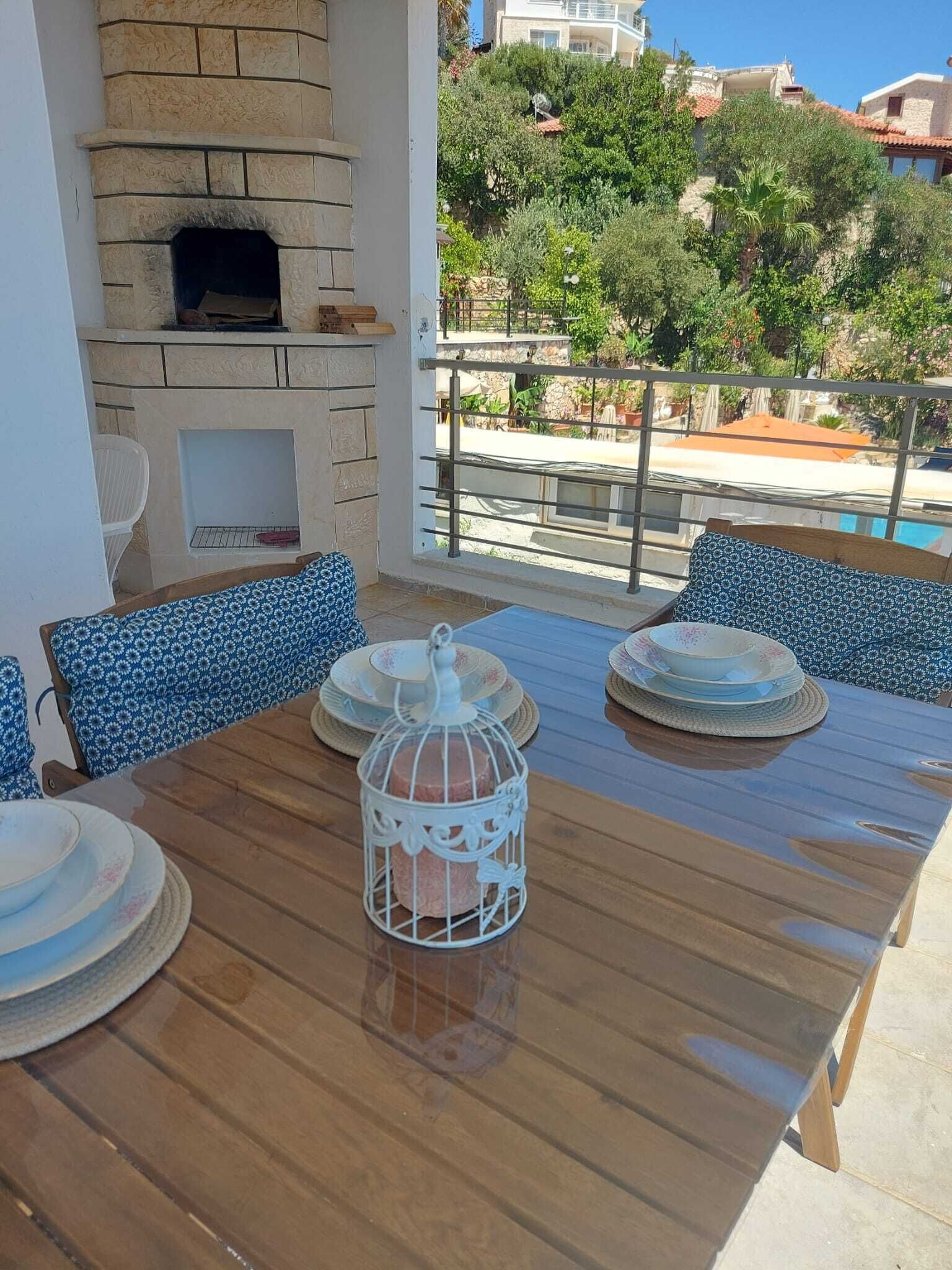 Une table en bois avec des chaises, une cage à oiseaux blanche et une cheminée en pierre.
