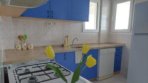 A kitchen with blue cabinets, a gas stove, a dishwasher, and a vase with flowers on the counter.