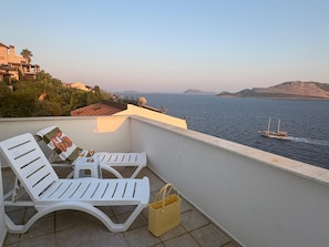 A balcony with white lounge chairs, a small table with a glass, and a yellow bag.
