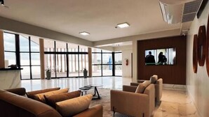 A spacious lobby with a large sofa, a smaller armchair, a coffee table, and a TV screen. - Rota Hotéis Rio Verde (Rio Verde)