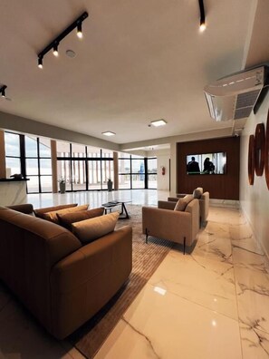 A spacious lobby with a large sofa, a smaller armchair, a coffee table, and a TV screen.