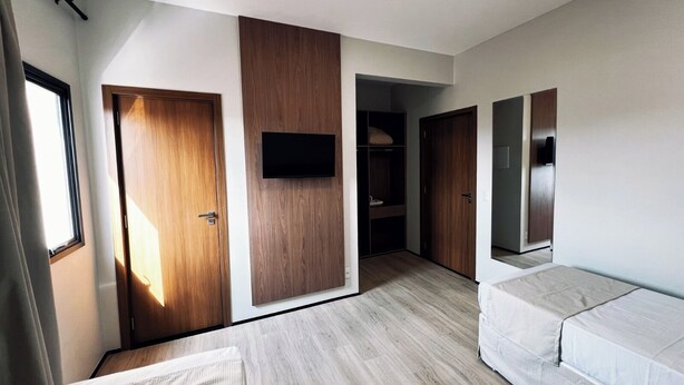 A modern bedroom with a wooden wardrobe, a built-in TV, and a sofa. - Rota Hotéis Rio Verde (Rio Verde)