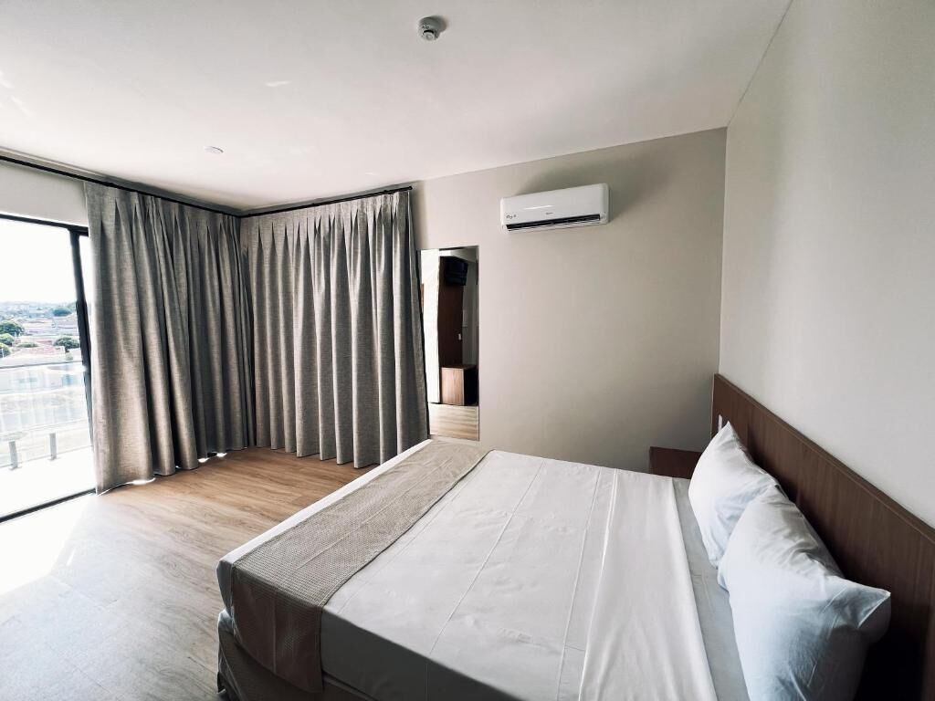 Ein Hotelzimmer mit einem großen Bett, einem fenster mit Vorhängen, einer Klimaanlage und Blick ins Freie.