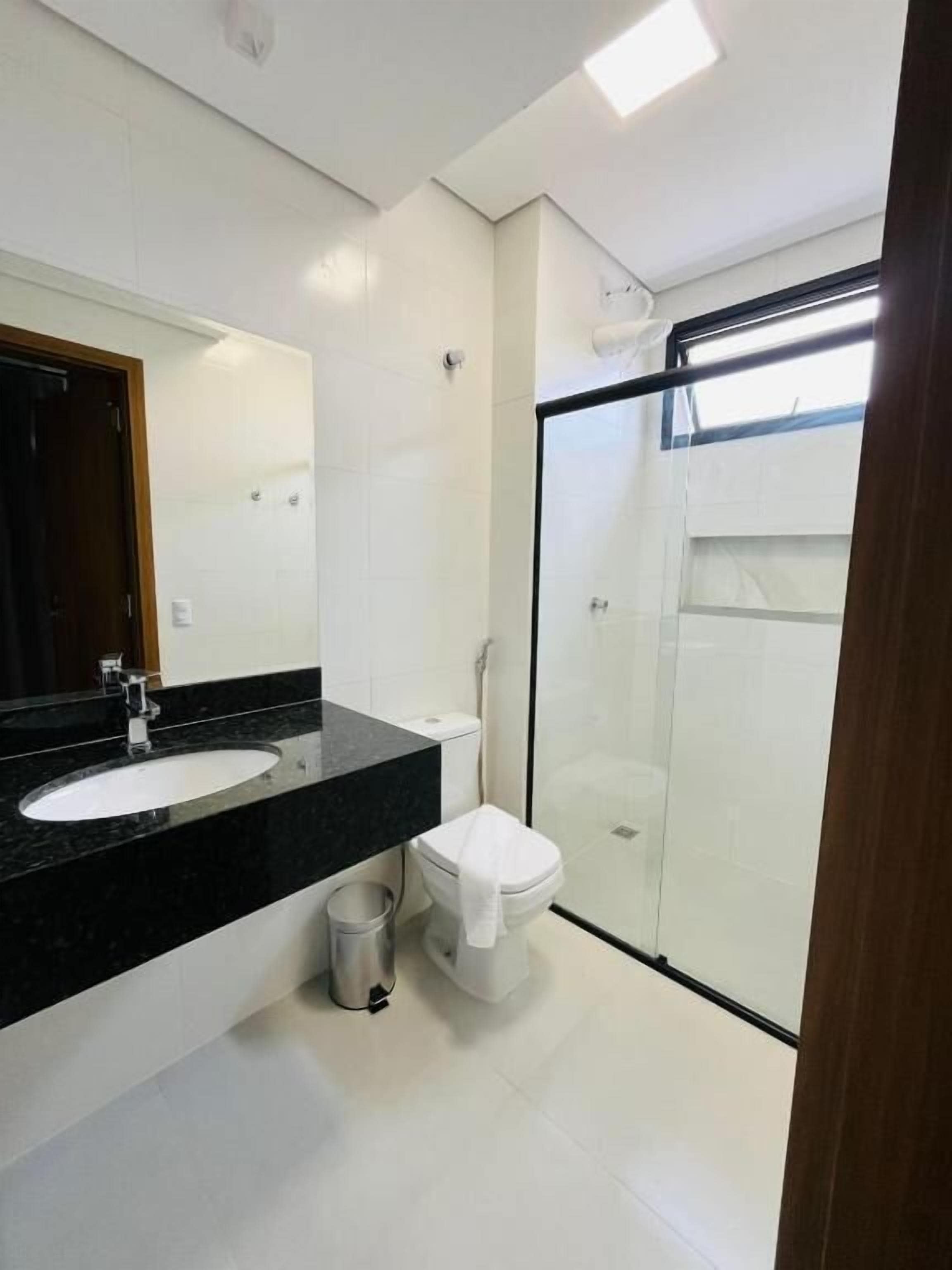 Un baño moderno con lavamanos de superficie negra, inodoro blanco y cabina de ducha de vidrio.