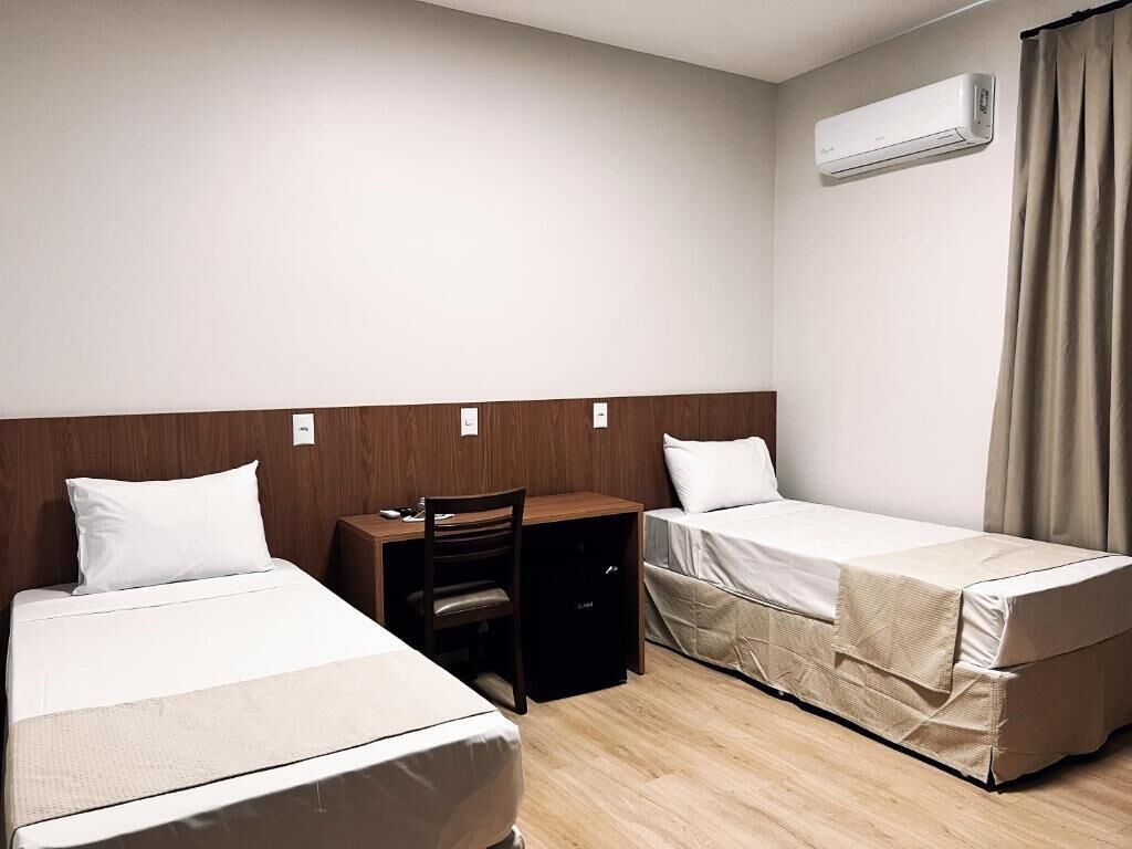 Quarto de hotel com duas camas, uma mesa, uma cadeira e ar condicionado.