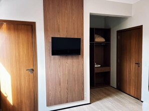 Ein Zimmer mit einem Holzschrank, einem an der Wand befestigten Fernseher und einem Schrank mit Regalen.