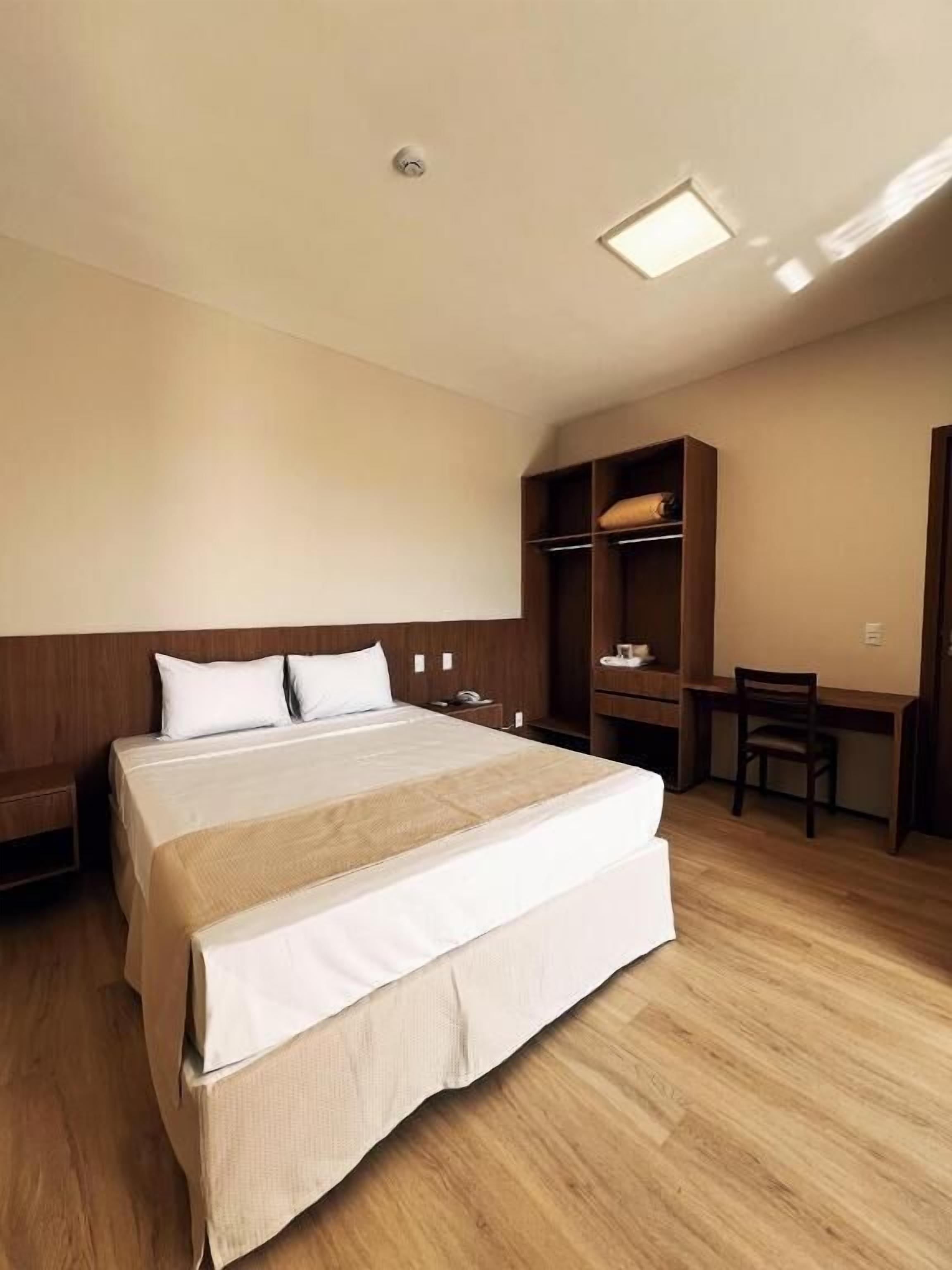 A hotel room with a large bed, a desk, and a chair.