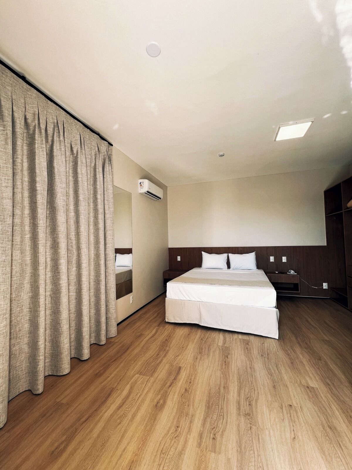 A hotel room with a bed, a nightstand, a wardrobe, a mirror, and an air conditioning unit.
