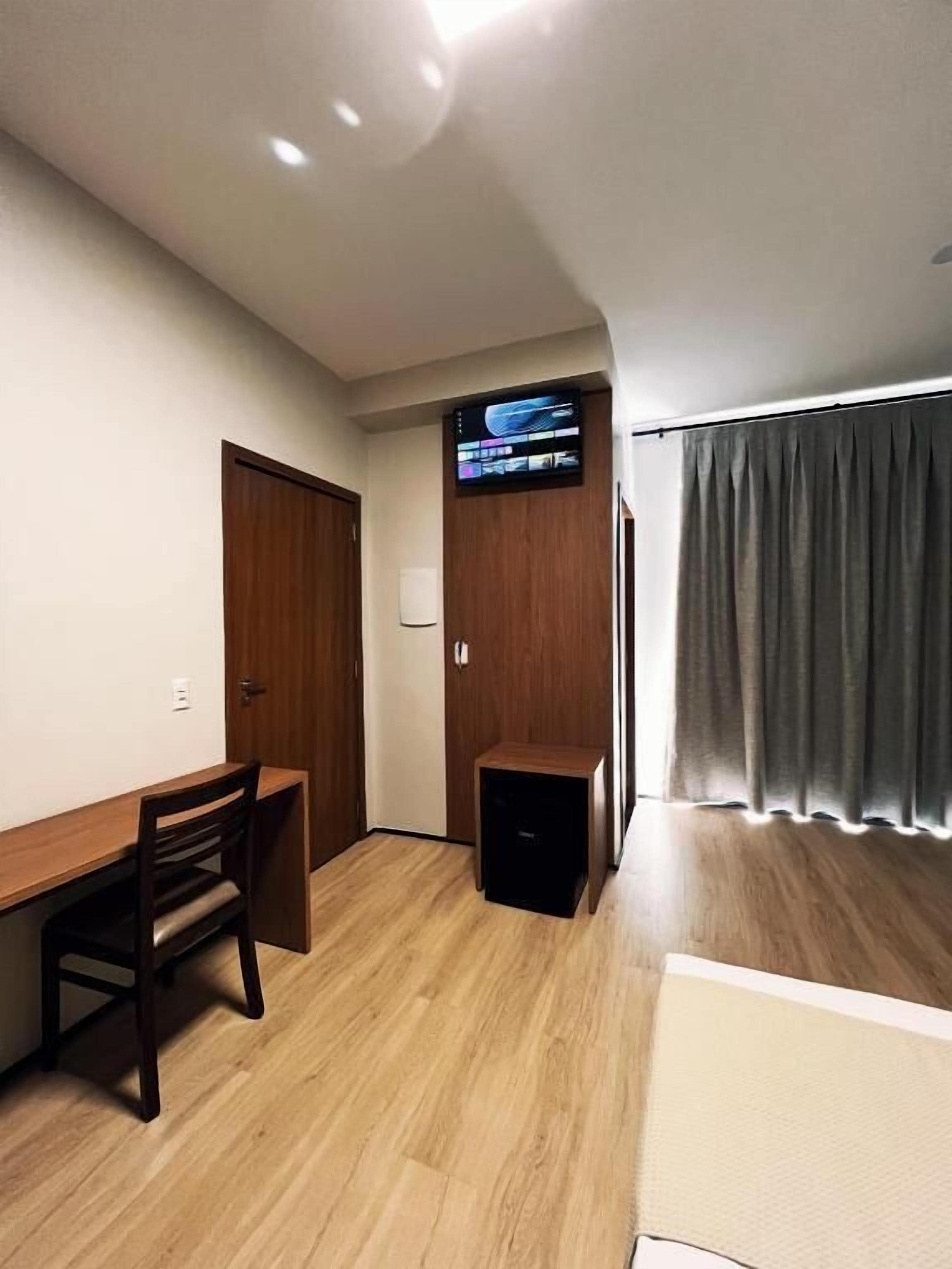 A room with a desk, chair, and a television mounted on the wall.