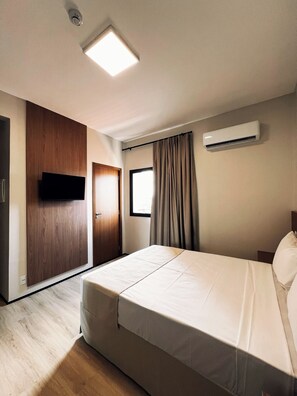 Ein Hotelzimmer mit Bett, Kleiderschrank, Fernseher, Klimaanlage und einem fenster mit Vorhängen.