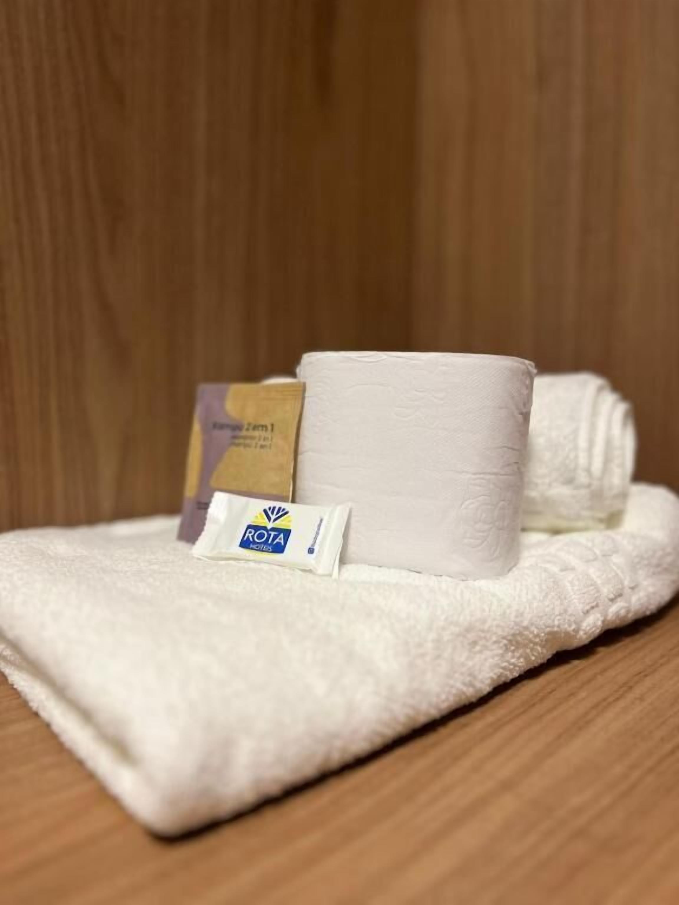 A white towel, a rolled-up towel, and a Rota tissue box on a wooden surface.