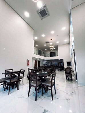 A spacious dining area with multiple tables and chairs, a fire extinguisher on the wall, and a modern ceiling design with recessed lighting.