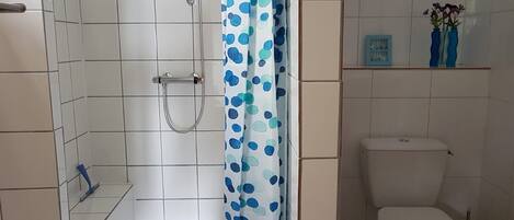 A bathroom with white tiles, a shower with a curtain, a toilet, and a shelf with vases.