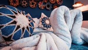 Una stanza accogliente con una coperta azzurro-bianca a motivi decorativi, una palla all'uncinetto e cuscini ornamentali su una parete scura.