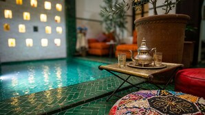 Zona piscina con un vassoio decorativo, un teiera e dei bicchieri, una grande pianta in terracotta e un tappeto colorato.