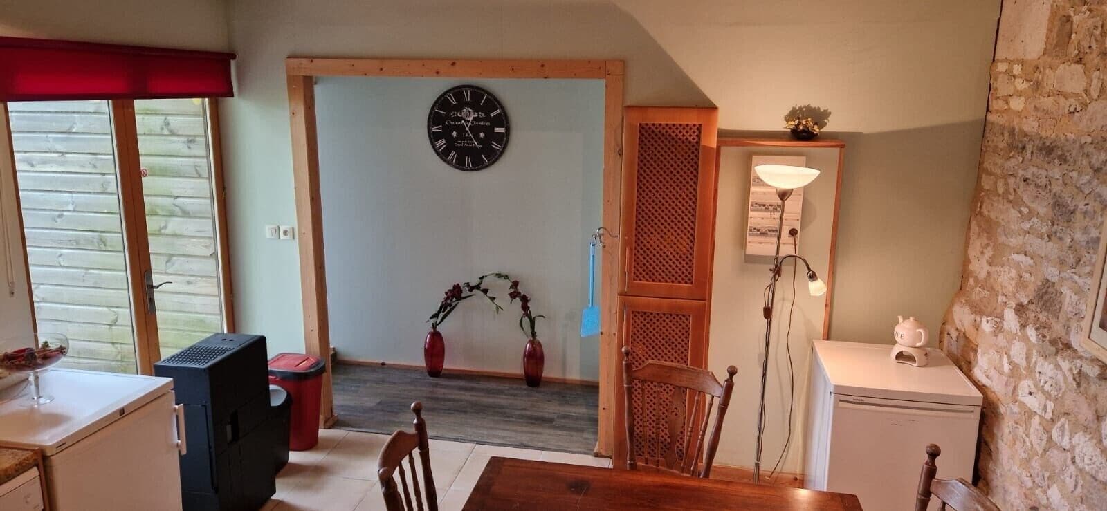 A room with a dining table, chairs, a clock on the wall, a lamp, and a small cabinet.