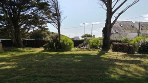 A grassy outdoor area with trees and a building in the background. - New Home 3-Min Walk to Beach & Large Garden (Piriac-sur-Mer)
