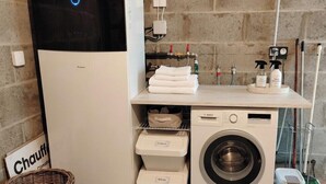 A compact laundry area with a Bosch washing machine, a drying machine, and neatly organized laundry baskets labeled 'Colours' and 'Whites'. - New Home 3-Min Walk to Beach & Large Garden (Piriac-sur-Mer)
