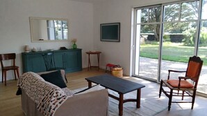 A living room with a sofa, a table, chairs, a cabinet, a mirror, and a view through large windows. - New Home 3-Min Walk to Beach & Large Garden (Piriac-sur-Mer)