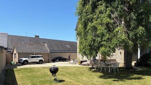 Een achtertuin met een barbecue, een witte SUV, een zwarte auto en een stenen gebouw.