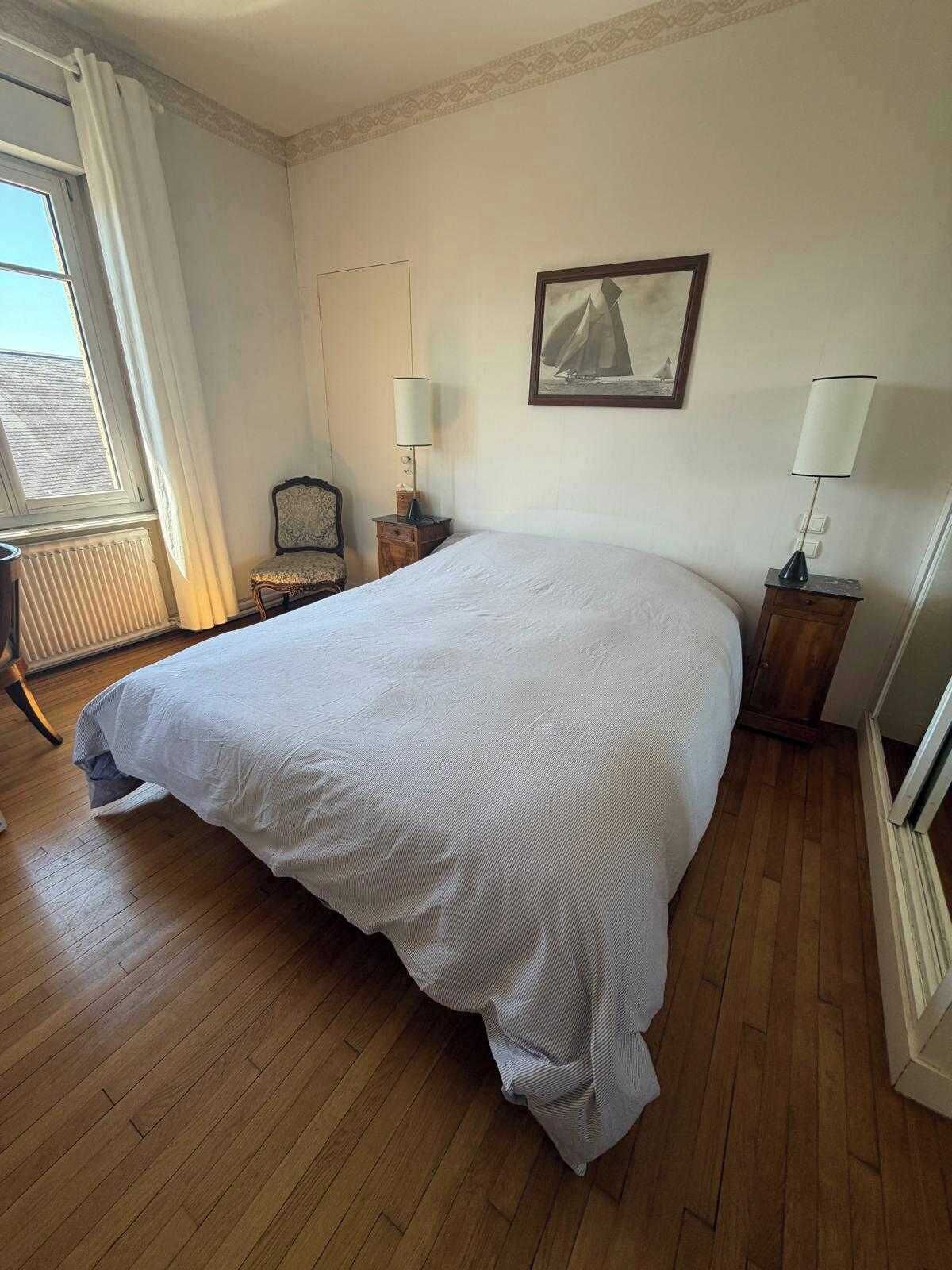 A hotel room with a large bed, a chair, a table, a lamp, a picture on the wall, and a window with curtains.