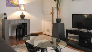 Een moderne woonkamer met een glazen salontafel, een bank, een televisie, een lamp en een plant.