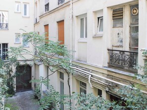 Un estrecho callejón entre edificios con un pequeño patio, que incluye una reja y plantas en macetas.