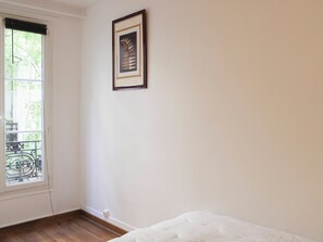Ein Zimmer mit einem Bett, einem Fenster mit Blick auf Grünflächen und einem gerahmten Bild an der Wand.