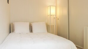 Een netjes opgemaakt bed met witte lakens in een kamer met een witte muur en een bedlampje.