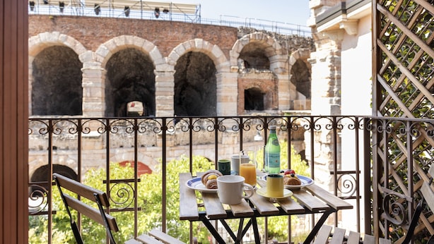 Ein Balkon mit Tisch, gedeckter Tisch für das Frühstück, eine Ziegelwand und ein schmiedeeisernes Geländer.
