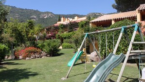 Un parque infantil con un tobogán y columpios en un área verde con montañas al fondo.