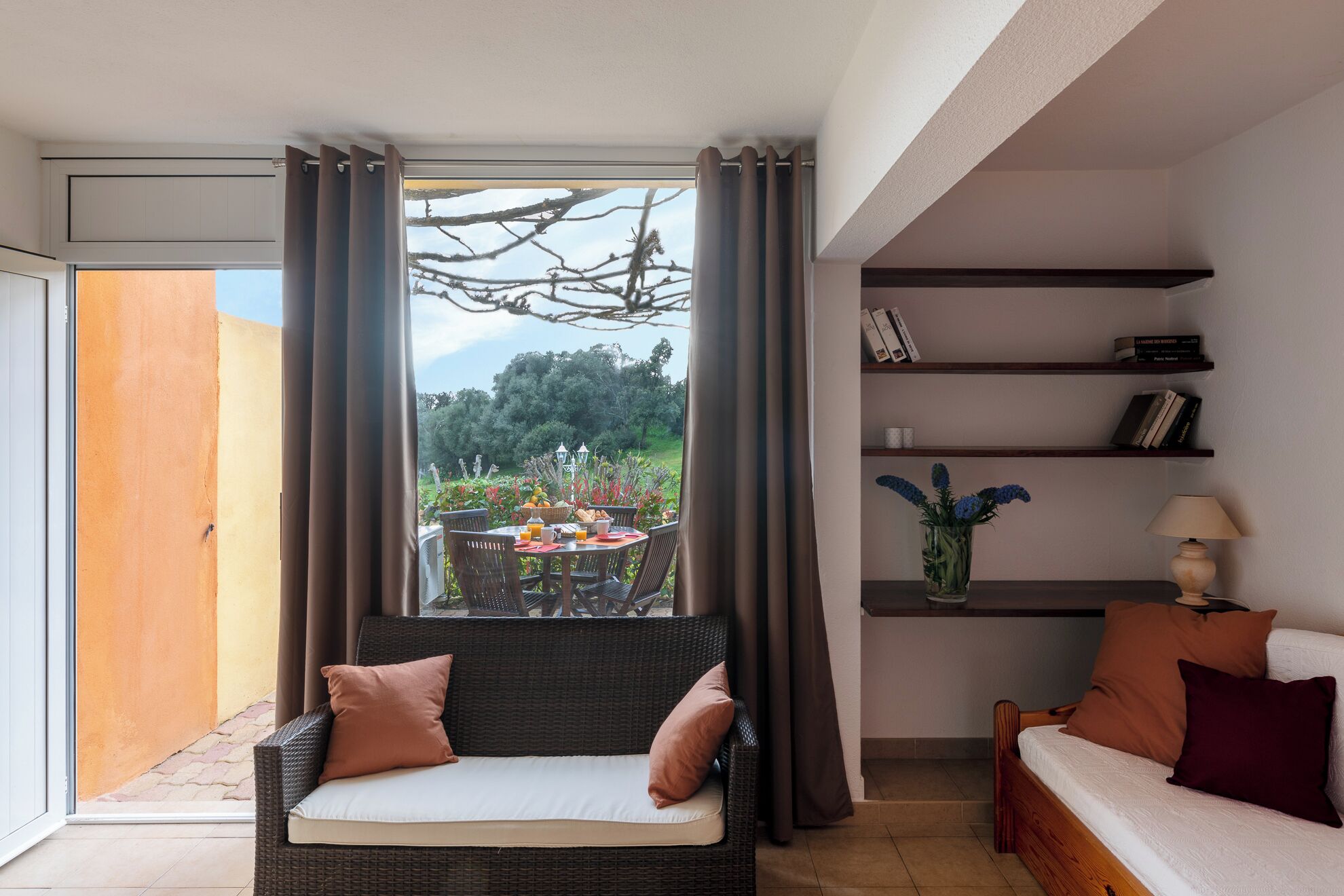 Una habitación con una mesa de comedor preparada para el desayuno, un sofá, una estantería y vistas al exterior.
